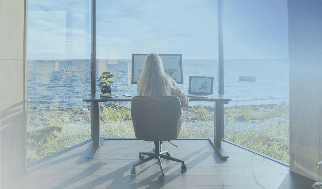 woman sitting behind an ergonomic height adjustable standing desk in a home office with a beautiful sea view