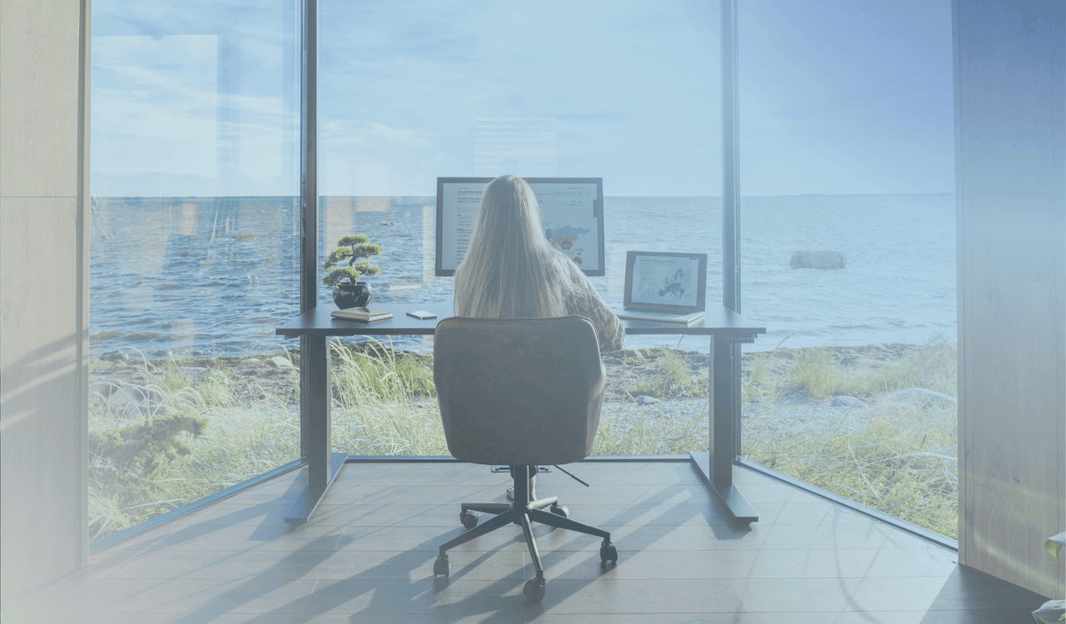woman sitting behind an ergonomic height adjustable standing desk in a home office with a beautiful sea view