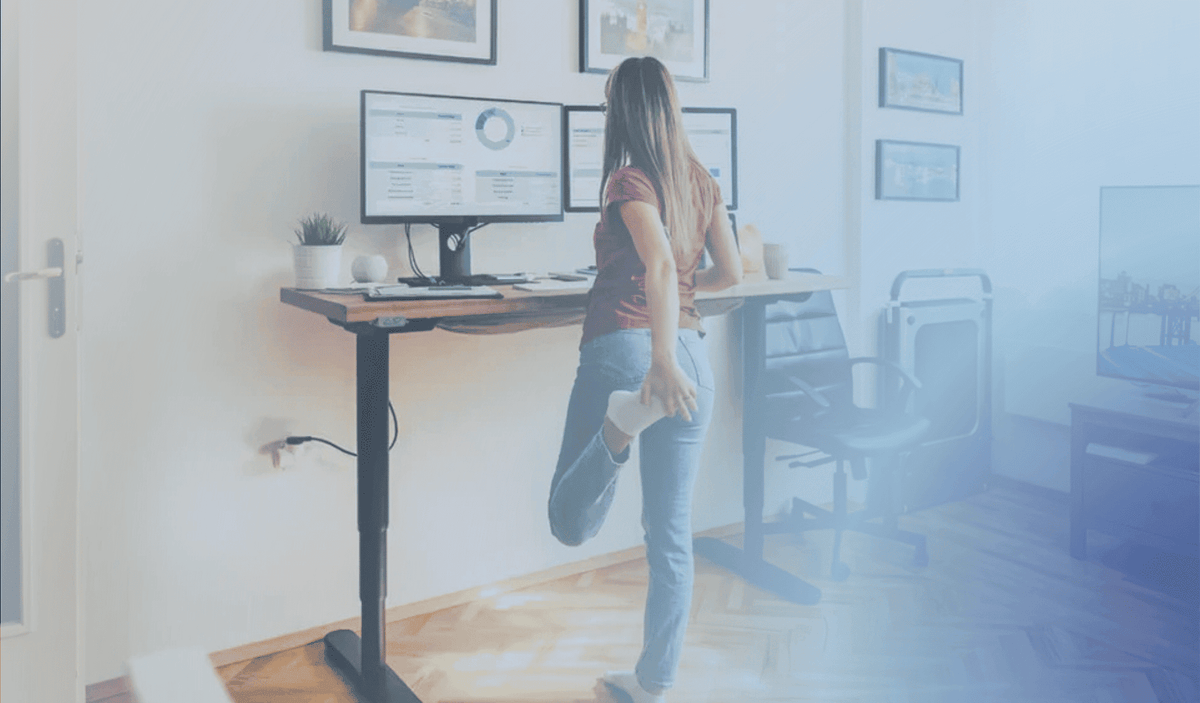 woman stretching in home office behind a standing desk while working