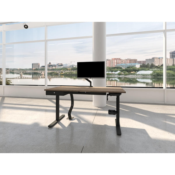 Wooden desk with a monitor in a modern office setting with large windows.