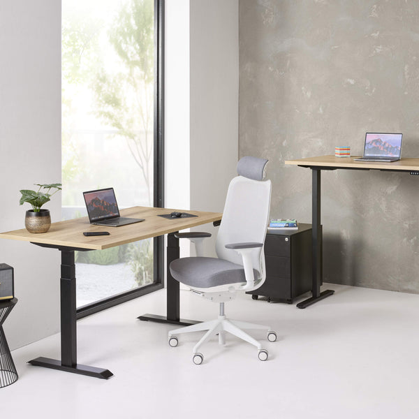 Modern office setup with adjustable desks and a chair in a bright room.