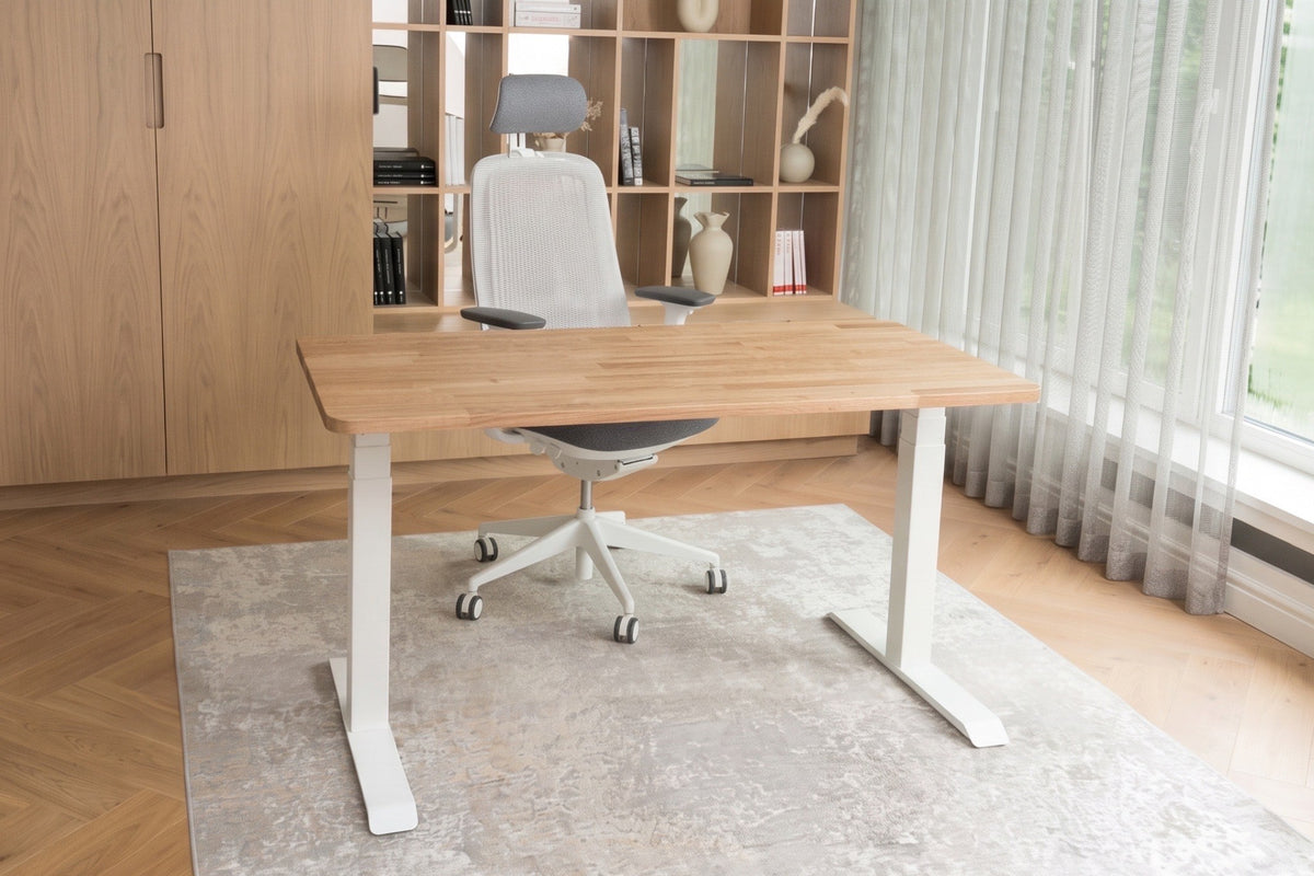 A modern standing desk with a solid oak wood top and white metal legs, in a bright home office with a white swivel chair.